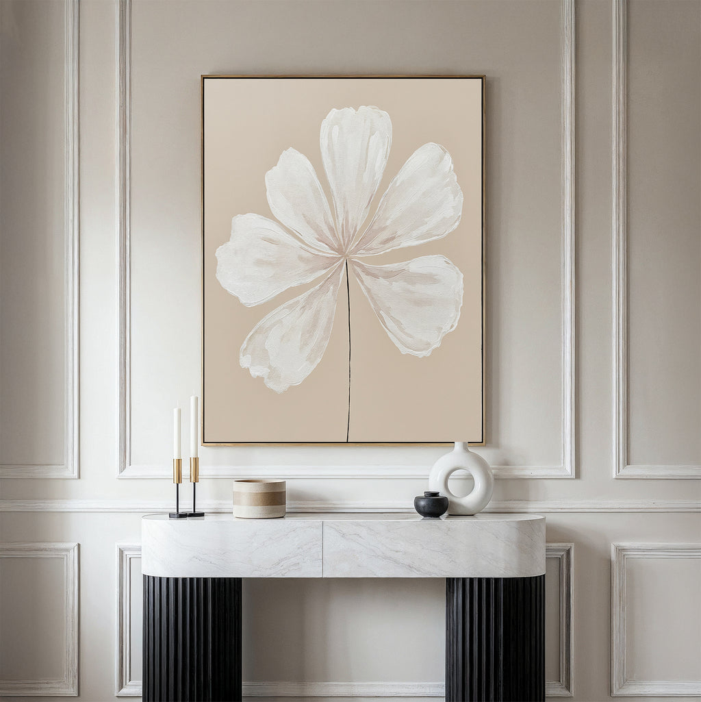 A minimalist interior showcases the Ivory Bloom Canvas Art - Vertical, a large beige botanical artwork of a white flower, mounted above a marble console table adorned with modern candles and geometric vases against an elegant paneled wall.