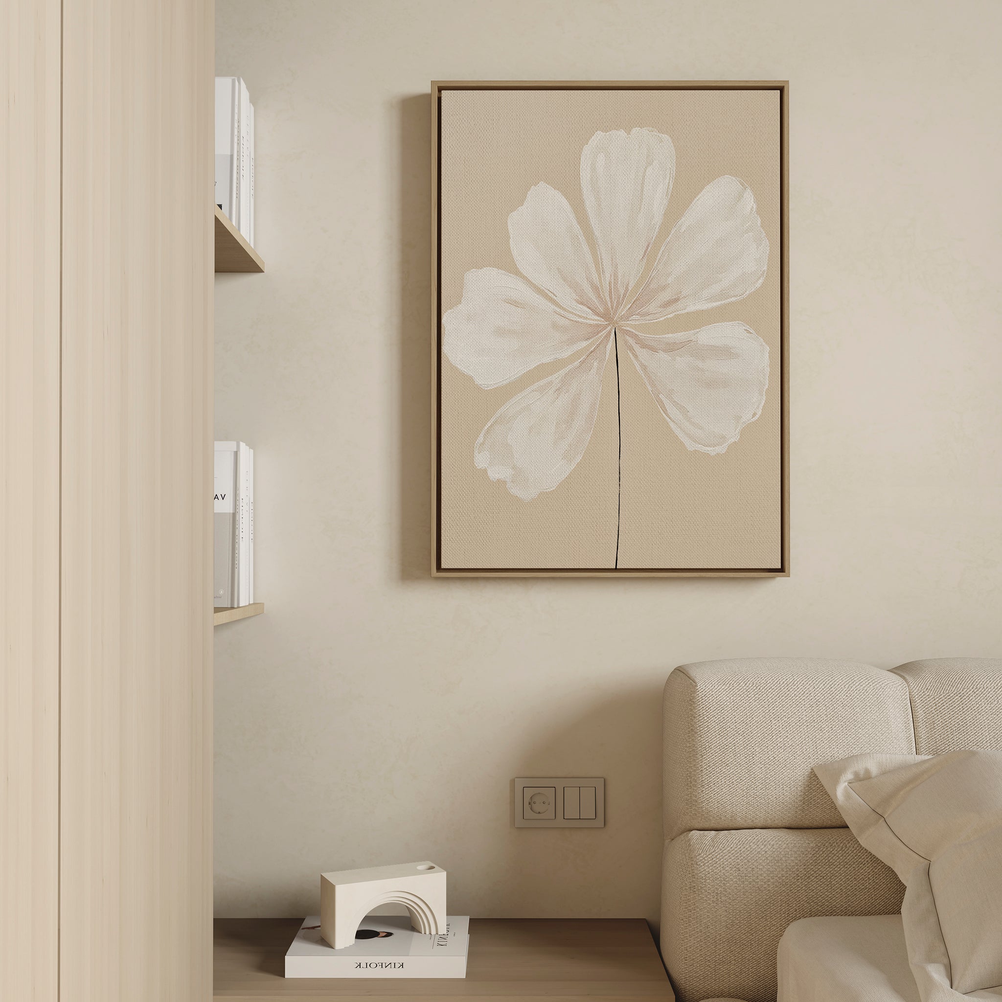 Minimalist living room with a beige wall, cream sofa, shelves of books, and the Ivory Bloom Canvas Art - Vertical: an elegant print featuring a white flower with delicate petals.