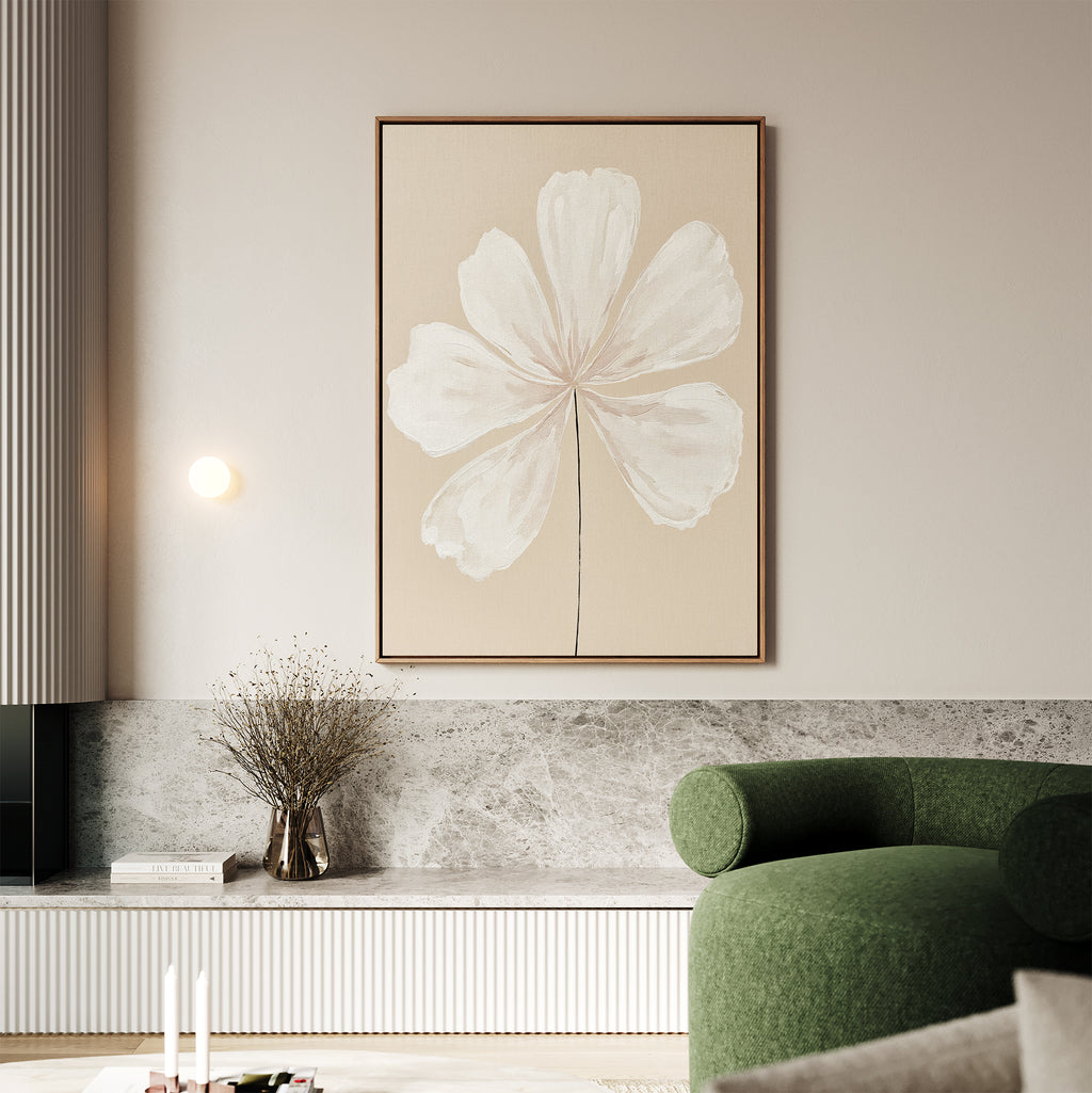 A modern living room featuring a green curved sofa, marble surfaces, neutral decor, a small vase of dried flowers, and the Ivory Bloom Canvas Art - Vertical—a large minimalist print of a white flower on beige.