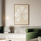 A modern living room featuring a green curved sofa, marble surfaces, neutral decor, a small vase of dried flowers, and the Ivory Bloom Canvas Art - Vertical—a large minimalist print of a white flower on beige.