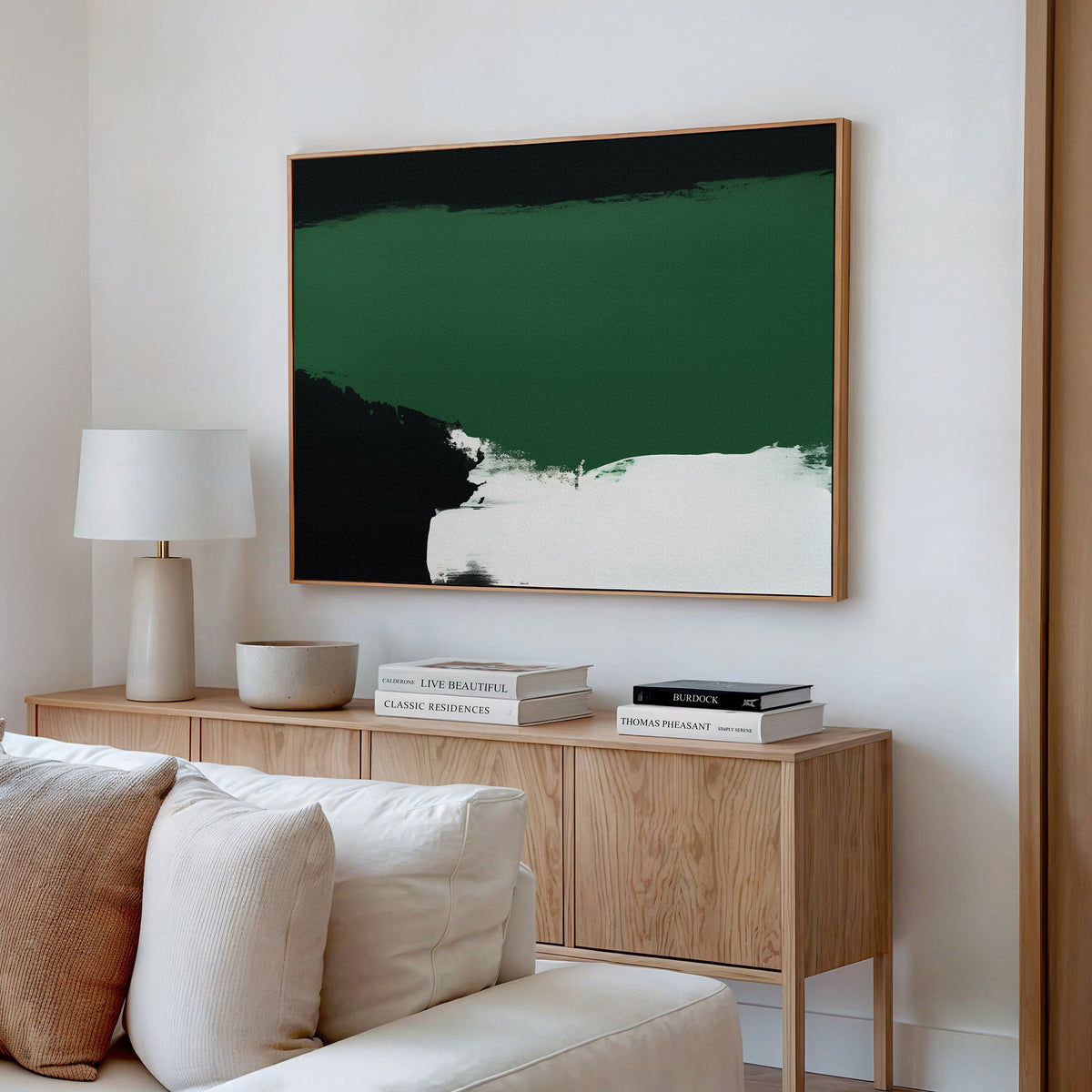 A modern living room featuring a light wood sideboard, neutral decor, a white table lamp, and Jade Depths Canvas Art - Horizontal—a large abstract painting in green, black, and white—hanging above.