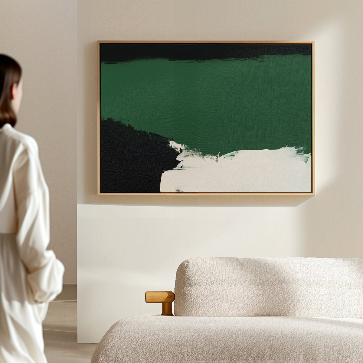 A person in a white shirt stands in a sunlit, minimal room, admiring the Jade Depths Canvas Art - Horizontal with green, black, and white sections displayed above a beige sofa.