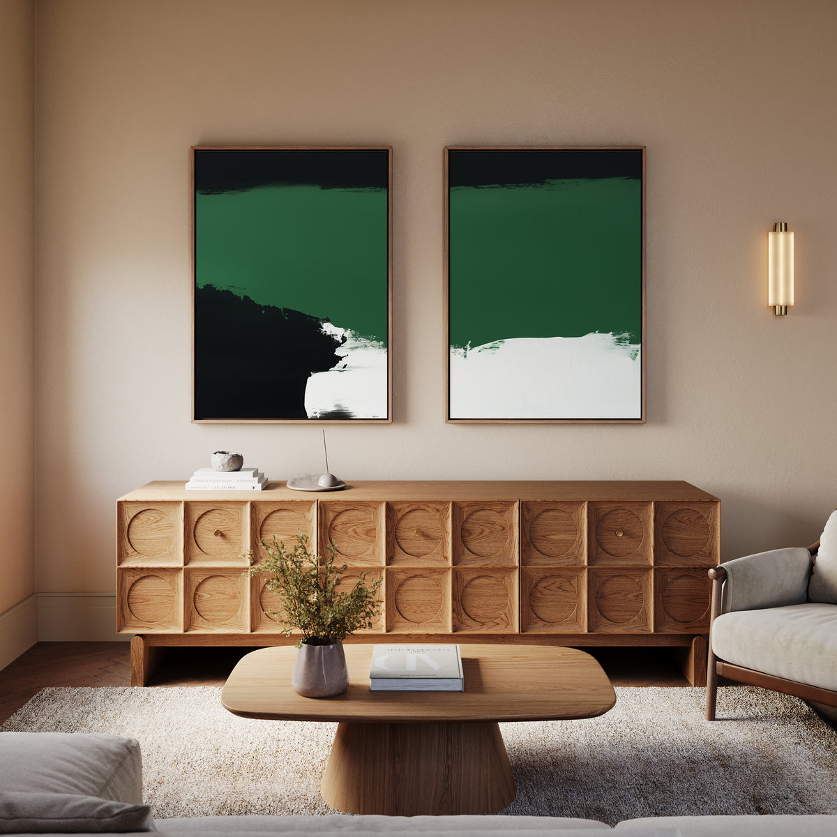 A modern living room with a wooden sideboard, “Jade Depths - Set Of 2” emerald green wall art above black artworks, a round wood coffee table with a vase and book, gray armchair, and wall sconce—a perfect modern space.