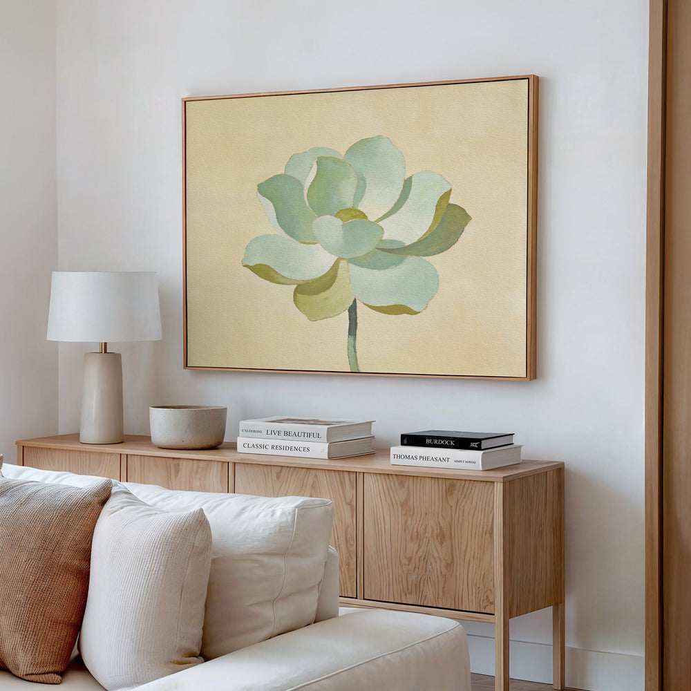 A minimal living room features a light wood sideboard with books, a white lamp, and a bowl. Above it hangs the Jade Reflection Canvas Art - Horizontal, adding sage green decor. A cream sofa is partially visible in front.