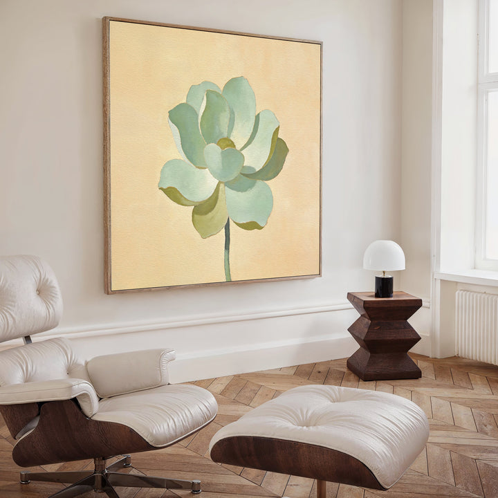 A modern living room with a cream lounge chair and ottoman, a wooden side table with a white lamp, and the Jade Reflection Canvas Art - Square featuring a green flower on beige in a Nordic-inspired minimalist style.
