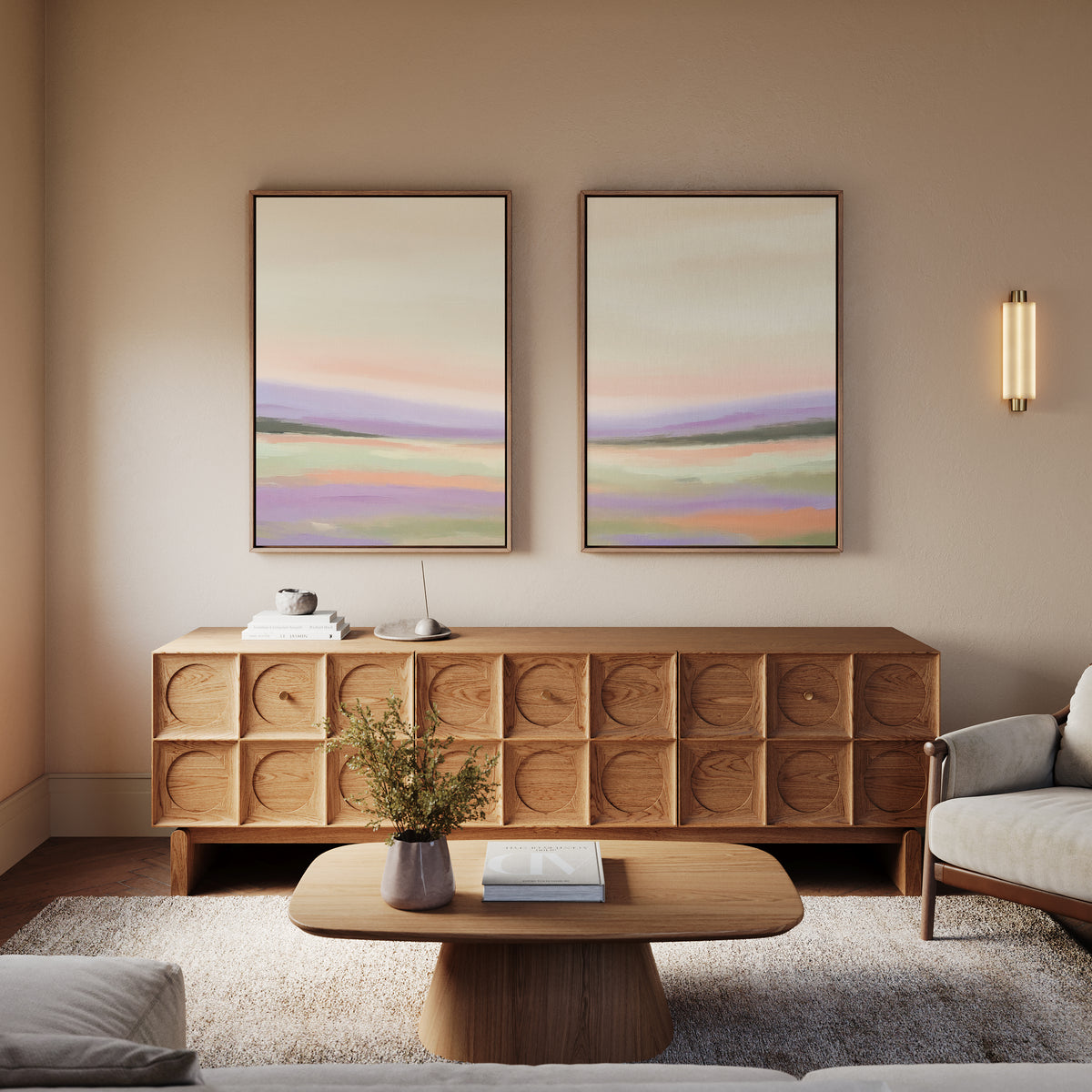 A cozy living room with a modern sofa, geometric wooden sideboard, and serene "Lavender Valley - Set Of 2" wall art above. A light wood coffee table holds a vase with greenery as soft lighting creates a warm, inviting atmosphere.