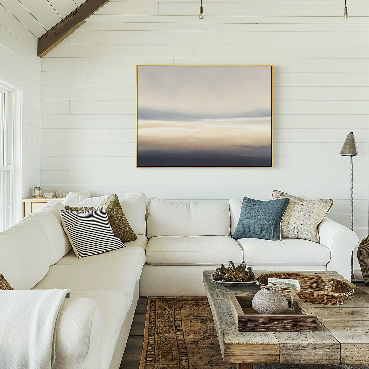 A cozy modern living room with white shiplap walls, a white sectional sofa with assorted pillows, a rustic wooden coffee table, and the Layered Dusk Canvas Art - Horizontal as calming wall décor above the couch.