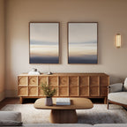 A modern living room features a wooden sideboard, matching coffee table, beige armchair, and Layered Dusk - Set Of 2 abstract wall art; a small vase with flowers on the table enhances the room’s contemporary charm.