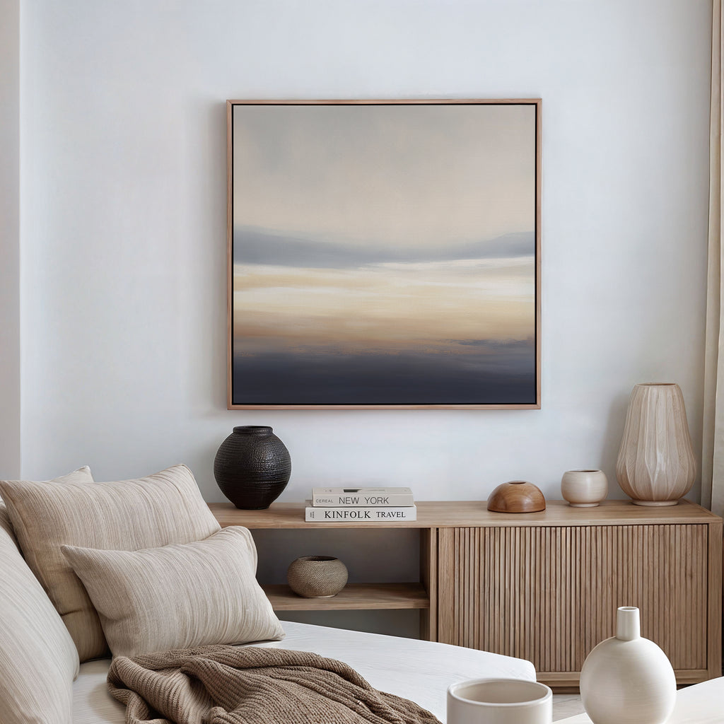 A minimalist living room with a beige sofa, striped cushions, a wooden sideboard with vases and books, and the Layered Dusk Canvas Art - Square in calming neutral tones displayed on a white wall.