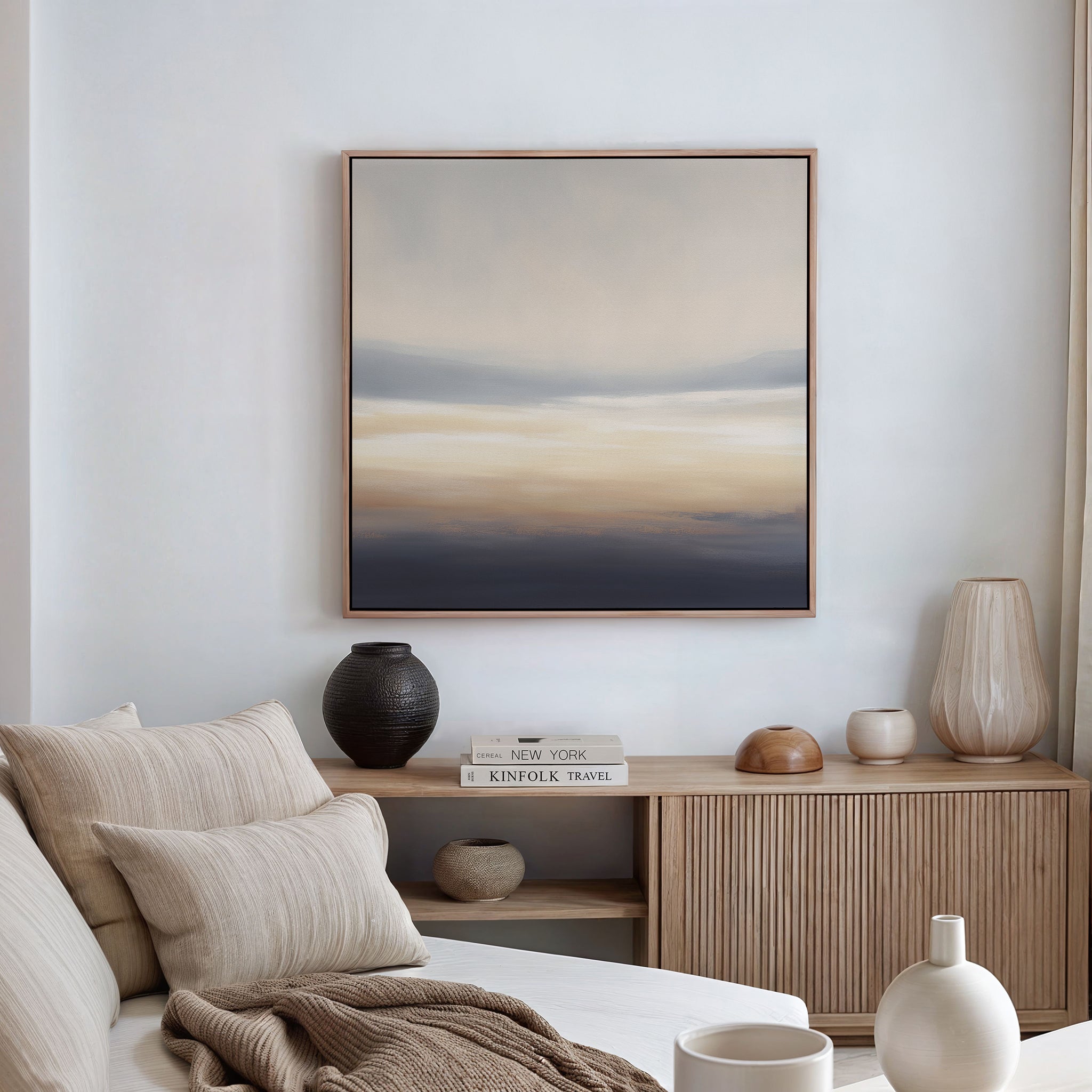 A minimalist living room with a beige sofa, striped cushions, a wooden sideboard with vases and books, and the Layered Dusk Canvas Art - Square in calming neutral tones displayed on a white wall.