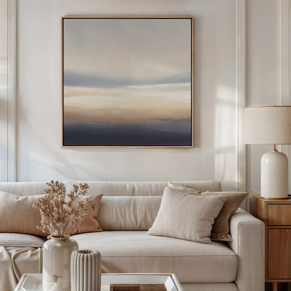 A modern living room with a beige sofa, neutral pillows, a side table with a ceramic lamp, dried flowers in a vase, and the calming Layered Dusk Canvas Art - Square hanging above the sofa.
