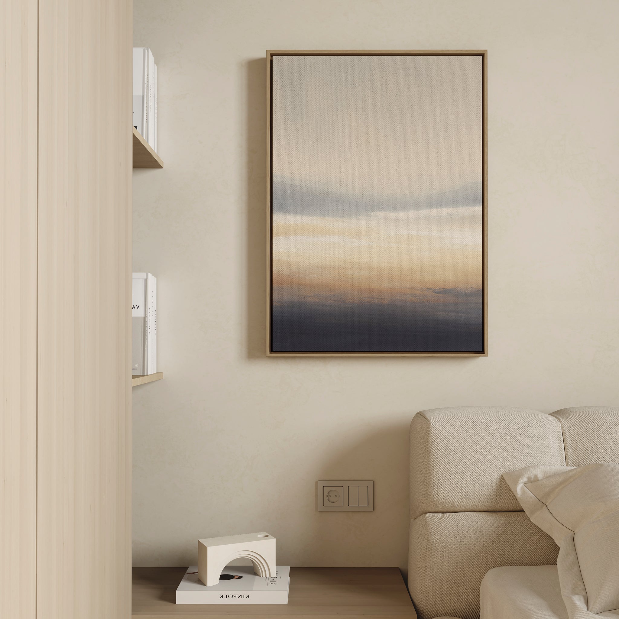 A modern living room corner with a beige sofa, light wood shelves with books, a small abstract sculpture, and Layered Dusk Canvas Art - Vertical featuring soft beige, blue, and orange tones hanging on the wall.