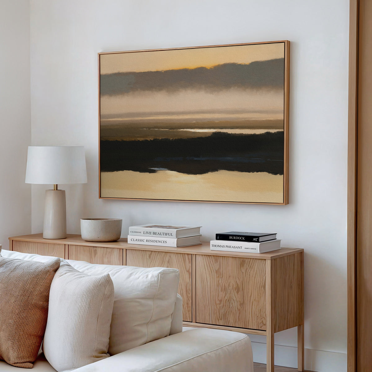 A modern living room features a wooden sideboard with stacked books, a white lamp, bowl, beige sofa, and serene decor highlighted by the Layered Valley Dawn Canvas Art - Horizontal in earthy tones above the sideboard.