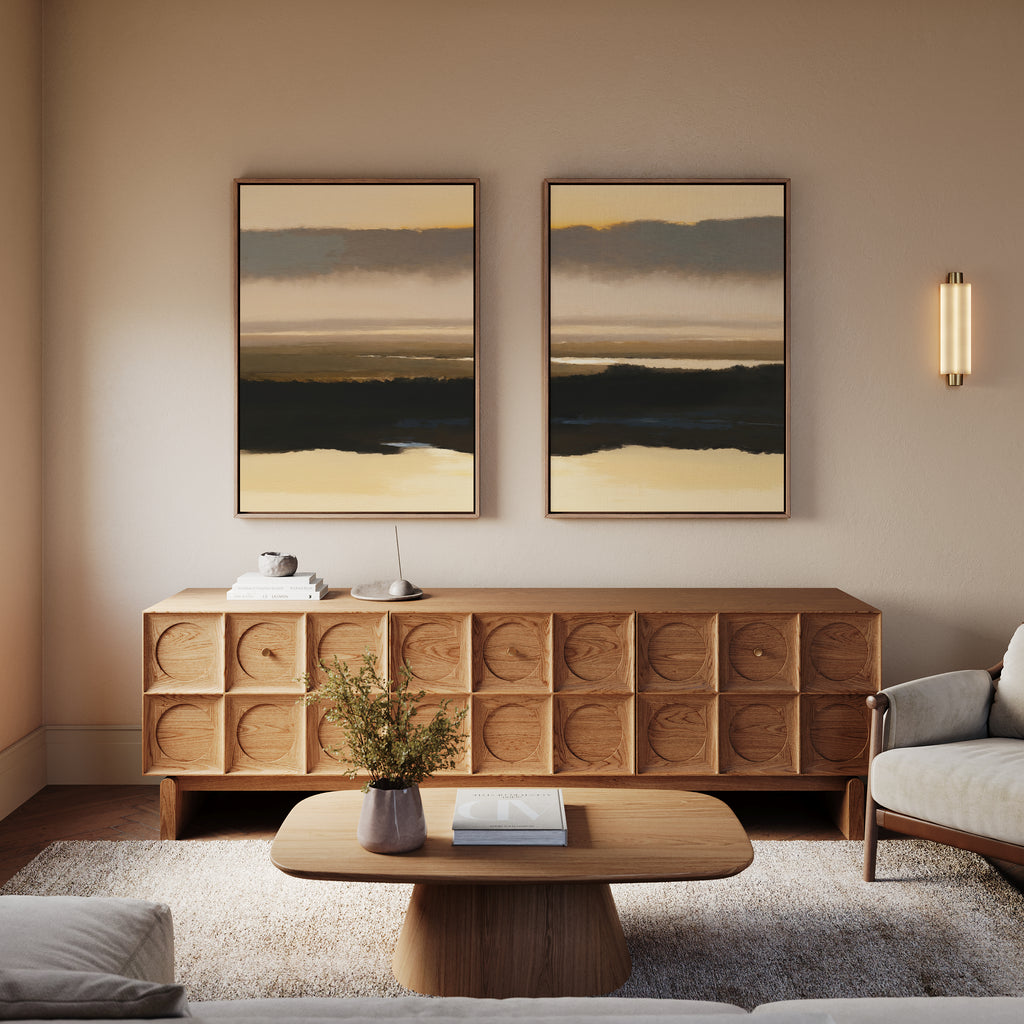 A cozy living room features a wooden cabinet, "Layered Valley Dawn - Set Of 2" landscape prints above it, a wooden coffee table with a vase of flowers and book, plus a light-colored sofa—all in soft, neutral hues.