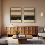 A cozy living room features a wooden cabinet, "Layered Valley Dawn - Set Of 2" landscape prints above it, a wooden coffee table with a vase of flowers and book, plus a light-colored sofa—all in soft, neutral hues.