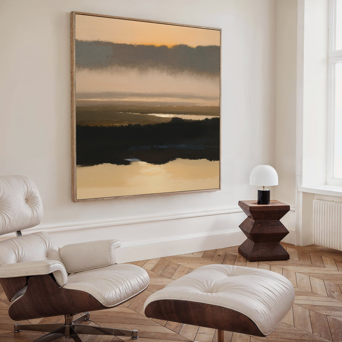 A modern living room with a white leather lounge chair and ottoman, a wooden side table with a white lamp, and the Layered Valley Dawn Canvas Art - Square creates a peaceful ambiance.