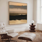 A modern living room with a white leather lounge chair and ottoman, a wooden side table with a white lamp, and the Layered Valley Dawn Canvas Art - Square creates a peaceful ambiance.