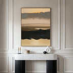 A minimalist console table with decor sits against a light wall, topped by the Layered Valley Dawn Canvas Art - Vertical, a serene abstract landscape in beige, black, and brown tones.