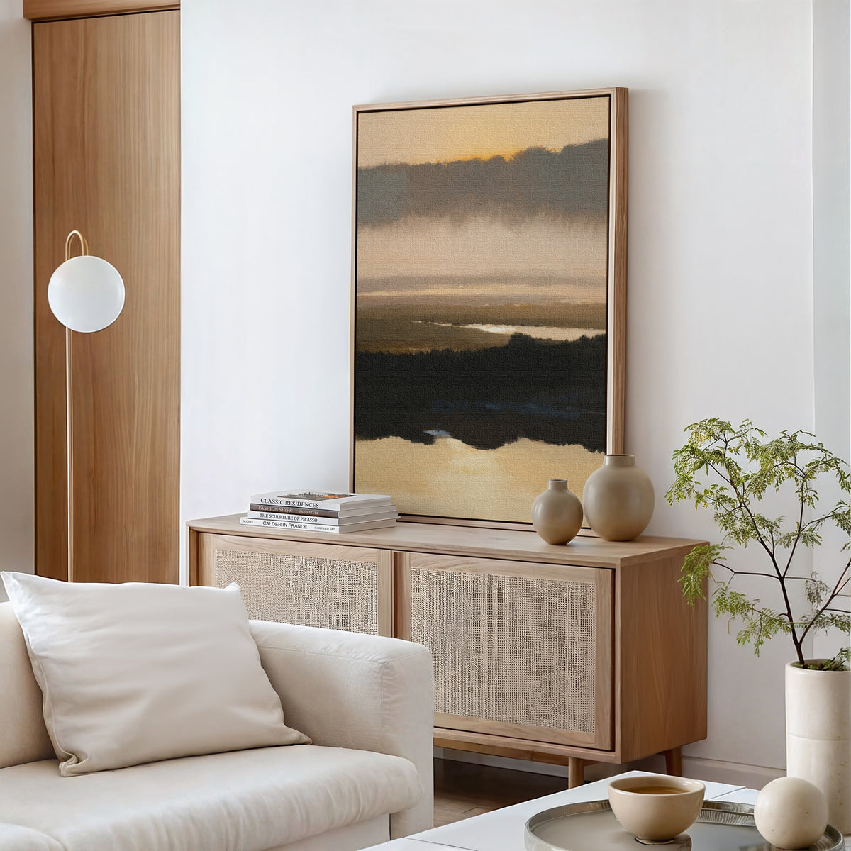 A modern living room featuring a light wood sideboard, Layered Valley Dawn Canvas Art - Vertical above, ceramic vases, a stack of books, round pendant lamp, white sofa, and a small green potted plant.