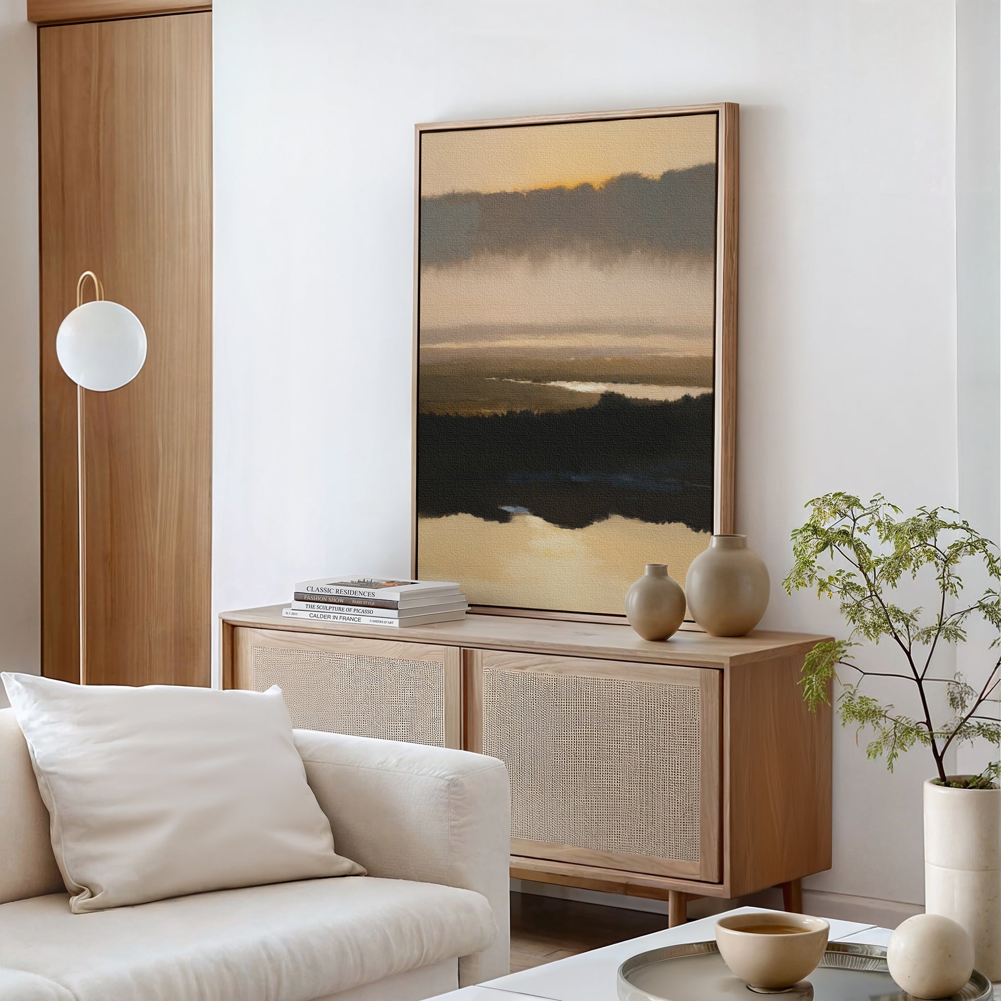 A modern living room featuring a light wood sideboard, Layered Valley Dawn Canvas Art - Vertical above, ceramic vases, a stack of books, round pendant lamp, white sofa, and a small green potted plant.