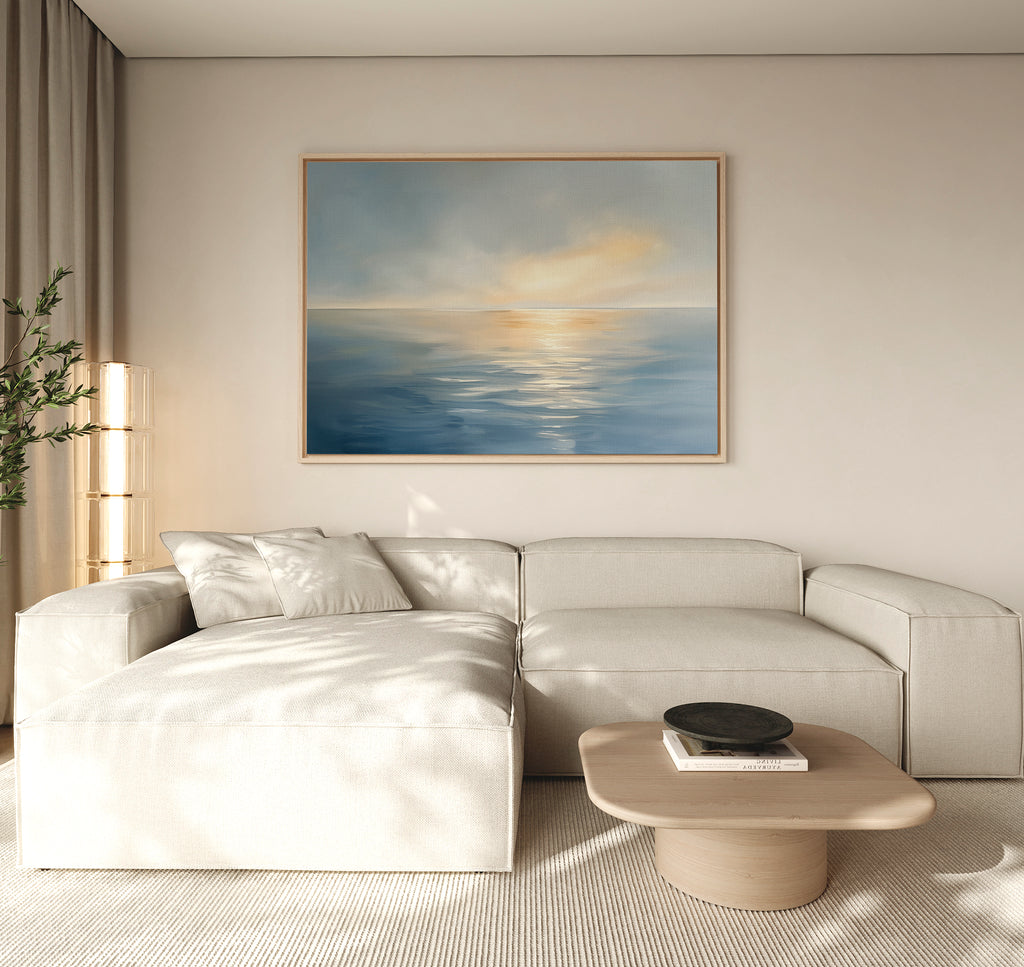 A modern living room with a beige sectional, light wood coffee table, tall lamp, potted plant, and the Luminous Calm Canvas Art - Horizontal in coastal blue and yellow tones creates a tranquil atmosphere on the wall.