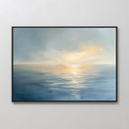 The Luminous Calm Canvas Art - Horizontal features a calm sea reflecting soft sunlight and a hazy sky in blue and warm yellow tones, framed in black and displayed on a plain white wall.