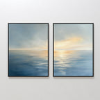 The "Luminous Calm - Set of 2" features framed canvas prints side by side, showing a tranquil ocean at sunrise or sunset with soft blue water, gentle waves, and warm orange-yellow hues reflecting from a cloudy coastal sky.