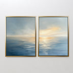 Luminous Calm - Set of 2: Two framed canvas prints feature a serene ocean in soft coastal hues, with hazy skies and golden light. Their minimal design brings a tranquil atmosphere when displayed together on a white wall.