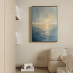 A minimalist living room with a light beige sofa, wooden bookshelf, and the Luminous Calm Canvas Art - Vertical showcasing a serene coastal sunrise or sunset scene adorning the wall.