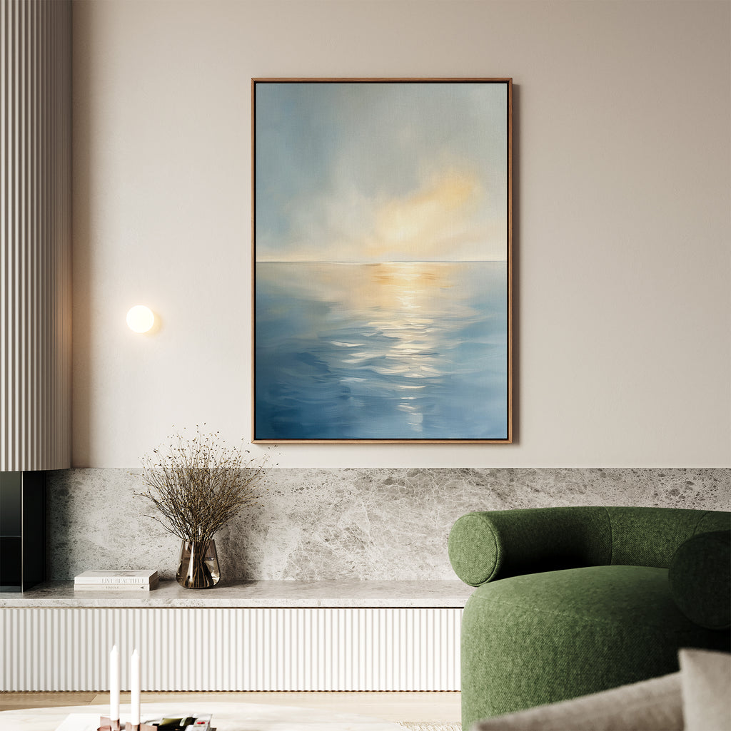 A modern living room features a green sofa, a marble ledge with a vase of dried branches, and the Luminous Calm Canvas Art - Vertical displaying a serene sea scene in soft coastal hues on the wall.
