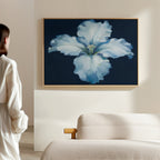 A person in a white shirt admires the Luminous Iris Canvas Art - Horizontal, featuring glowing white and blue petals against a dark background, displayed above a light-colored sofa on a beige wall.