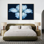 A modern bedroom features an olive green upholstered bed with white bedding, two beige lamps on round nightstands, and the Luminous Iris - Set of 2 blue flower canvas prints above the bed on a crisp white wall.