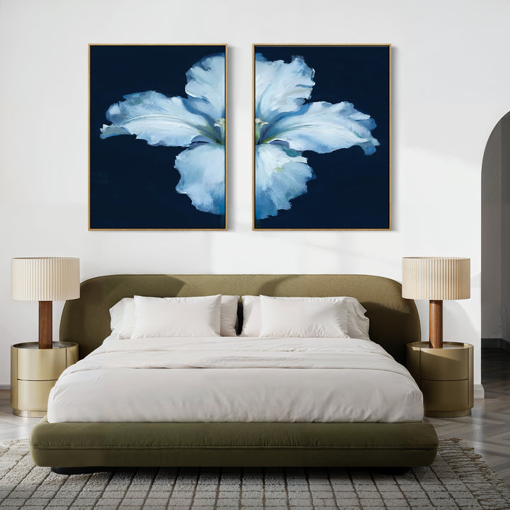 A modern bedroom features an olive green upholstered bed with white bedding, two beige lamps on round nightstands, and the Luminous Iris - Set of 2 blue flower canvas prints above the bed on a crisp white wall.