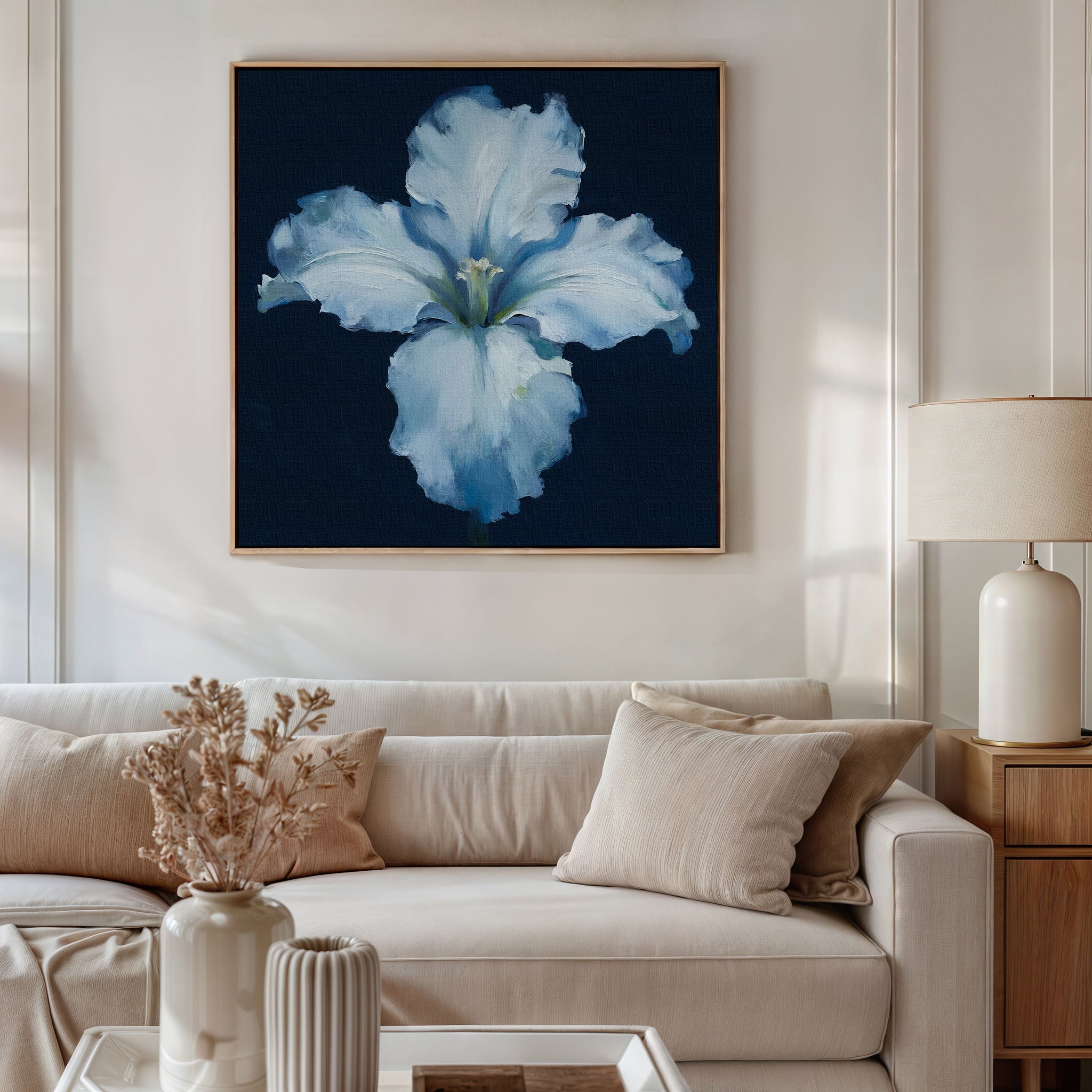 A modern living room with a white sofa, beige cushions, and a side table with a lamp features dried flowers in a vase and the Luminous Iris Canvas Art - Square from Nordic Park hanging on the wall.