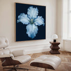 A modern living room with a white lounge chair and ottoman, wooden side table and lamp, and the Luminous Iris Canvas Art - Square in blue and white from Nordic Park displayed on the wall.