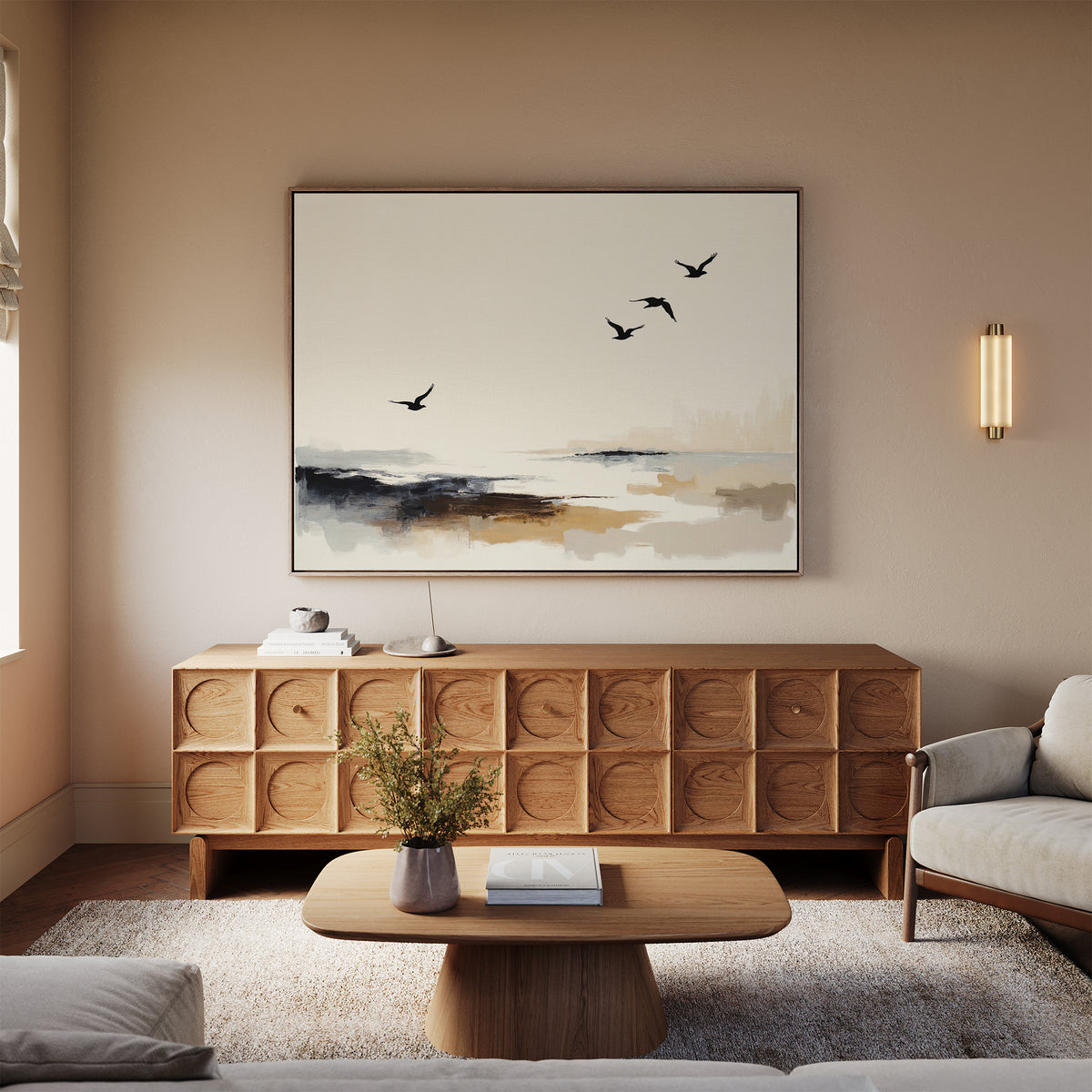 A minimalist living room features a wooden coffee table, textured sideboard, neutral sofa, and the Maritime Flight Canvas Art - Horizontal with birds over an abstract landscape. Warm lighting and soft beige walls add a cozy touch.