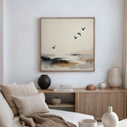 A minimalist living room with neutral tones features a beige sofa, wooden sideboard with ceramic vases and books, and the Maritime Flight Canvas Art - Square—a modern coastal painting of flying birds adding an airy touch to the space.