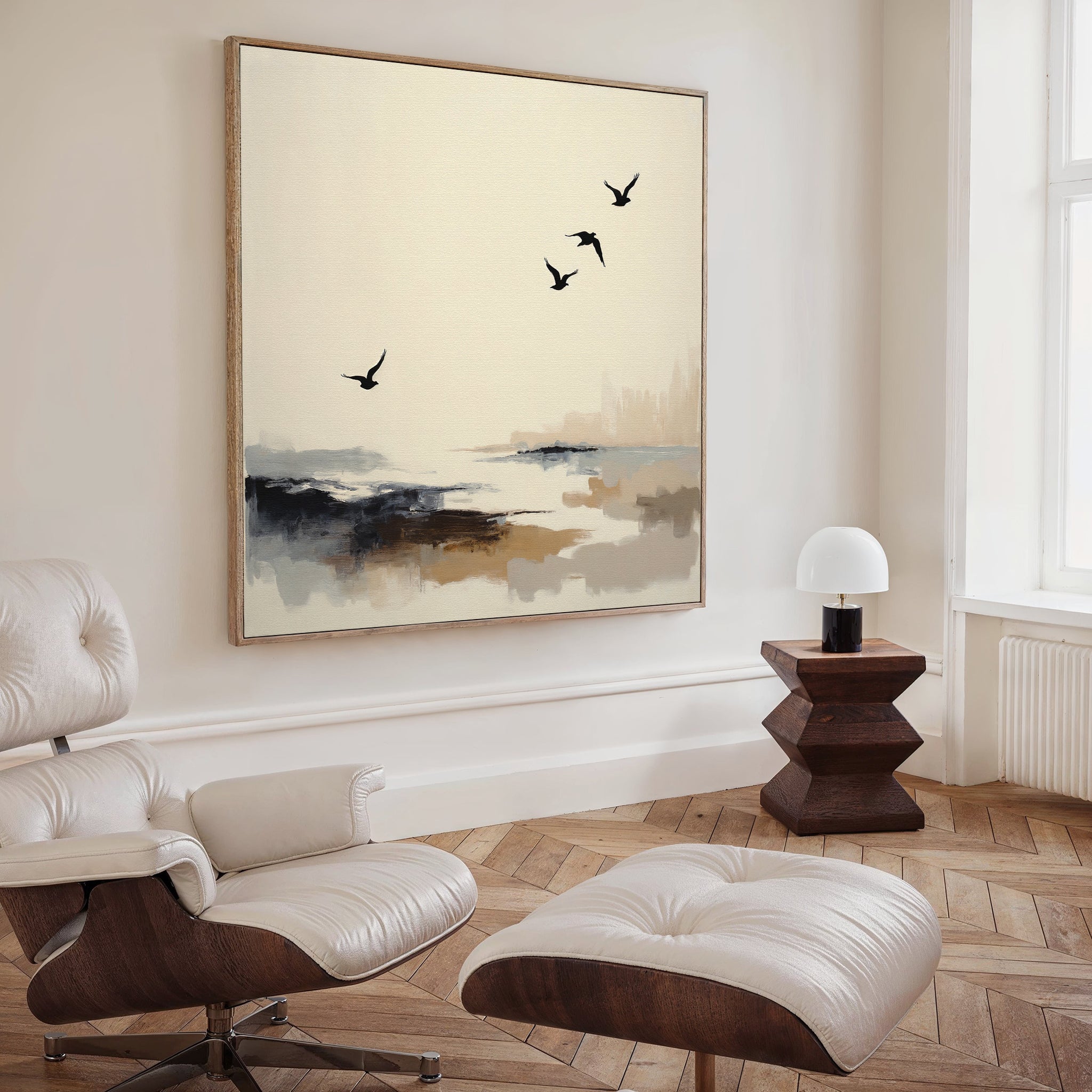 A modern, minimalist living room features a white lounge chair, ottoman, geometric wooden side table, small white lamp, and the Maritime Flight Canvas Art - Square, adding subtle nautical decor with birds soaring over an abstract coast.