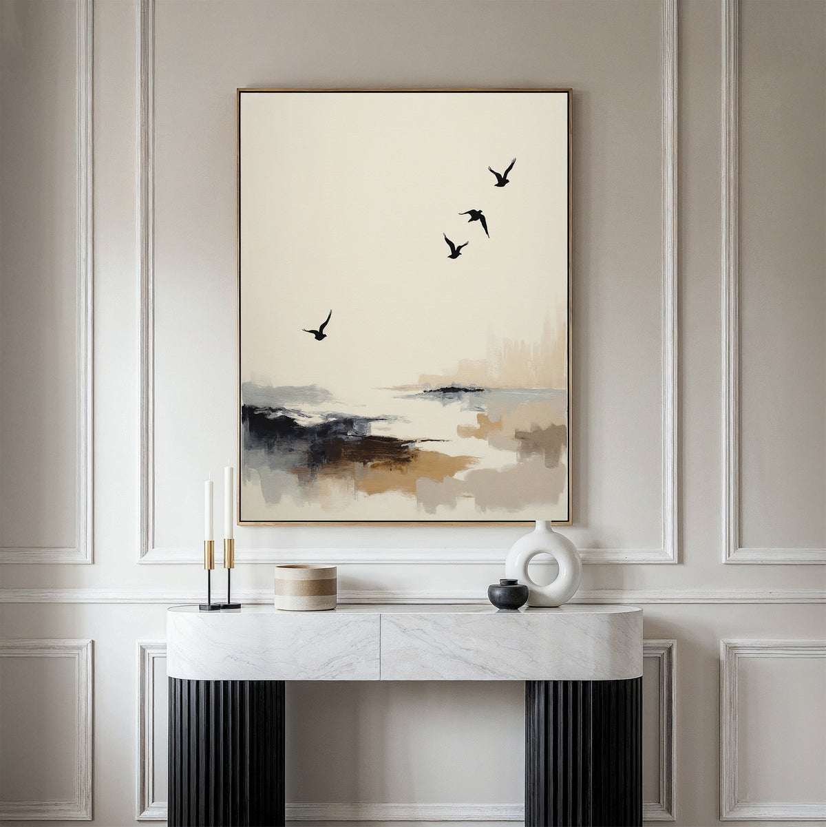 A minimalist room featuring a marble console table, decorative objects, and the Maritime Flight Canvas Art - Vertical, which depicts birds flying over an abstract landscape in neutral tones.