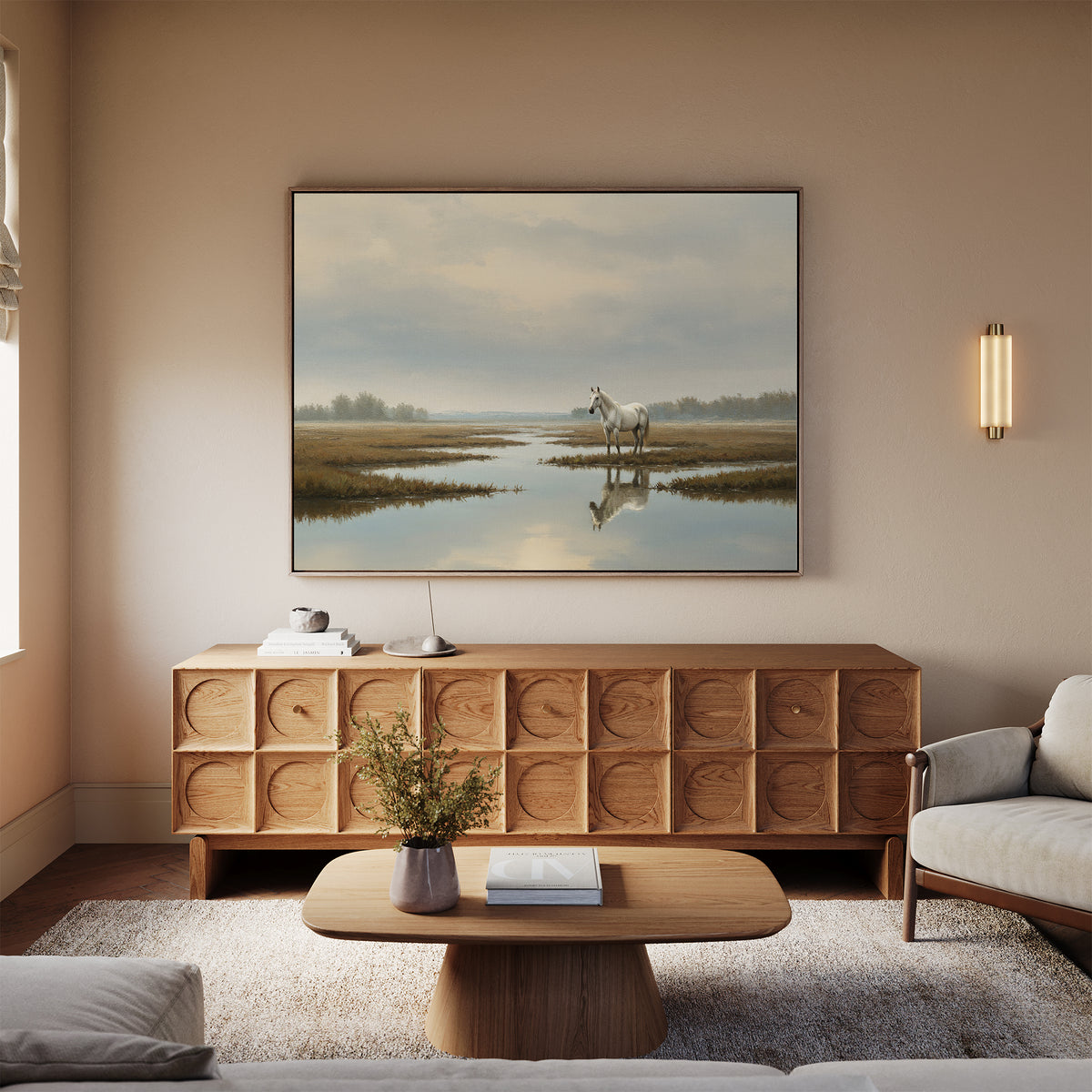 A cozy, neutral-toned living room features a wooden sideboard, coffee table, light sofa, and the Marsh Reflection Canvas Art - Horizontal—showing a majestic white horse by tranquil waters in a serene Nordic park.