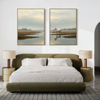A modern bedroom with an olive green bed, white bedding, two beige nightstands with matching lamps, and the Marsh Reflection - Set Of 2 landscape prints above the bed, including a serene image featuring a white horse by water.