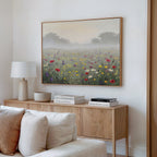 A cozy living room corner features a wooden sideboard, books, a lamp, and the Meadow Dreams Canvas Art - Horizontal as meadow wall art hanging above a cream-colored sofa.