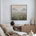A cozy living room with a beige sofa, neutral cushions, and a wooden sideboard. The Meadow Dreams Canvas Art - Square depicting a misty wildflower scene hangs above, adding charm. Decorative vases and books sit on the sideboard.