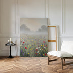 The Meadow Dreams Canvas Art - Vertical, depicting a wildflower meadow, leans against a white-paneled wall in a bright room with parquet flooring, a cushioned chair, and a small round table with candles and books.