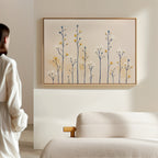 A person in a white shirt stands in a minimalistic room, gazing at the Meadow Symphony Canvas Art - Horizontal featuring delicate abstract yellow, blue, and white flowers above a beige textured sofa.