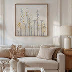 A modern living room with a white sofa, beige cushions, a wooden side table with a white lamp, and the Meadow Symphony Canvas Art - Square featuring minimalist blue and yellow flowers above the sofa for chic spring meadow decor.