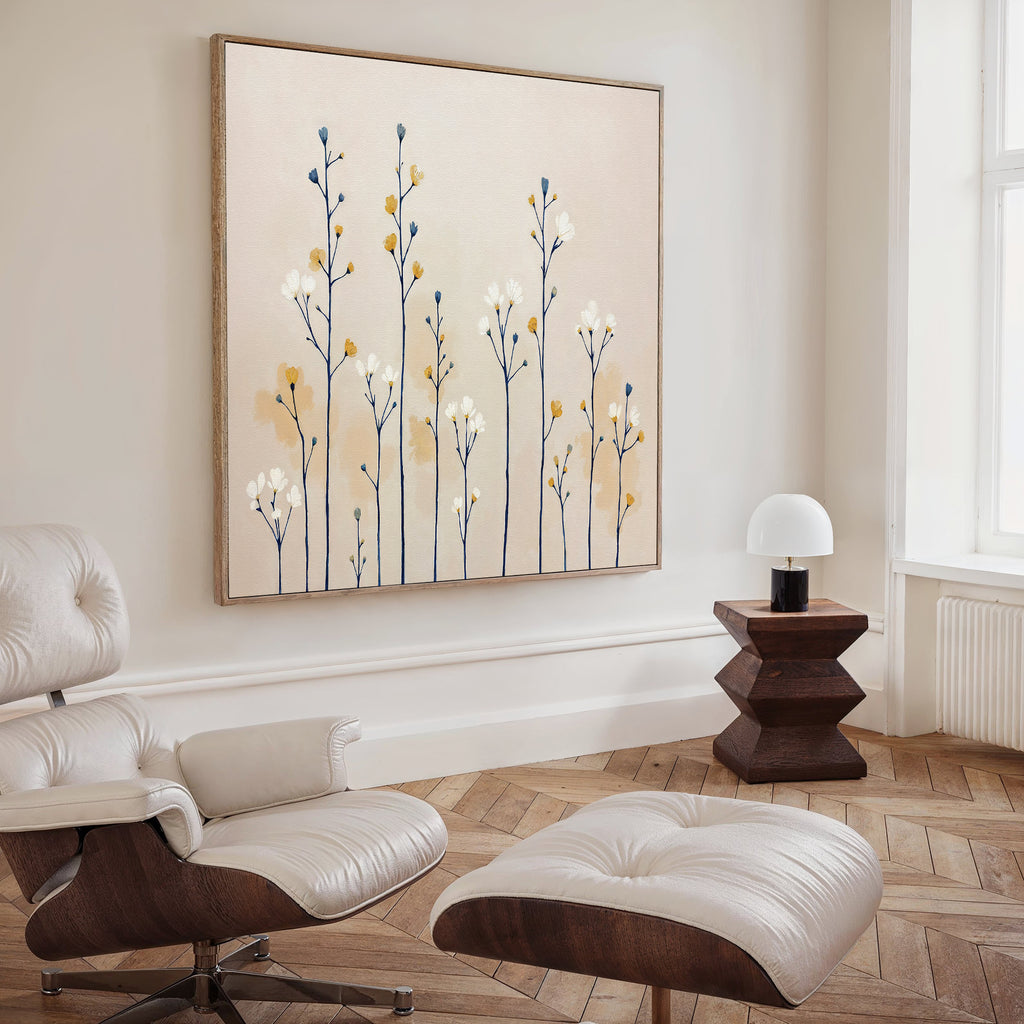A modern, minimal living room with a white lounge chair and ottoman, geometric wooden side table with lamp, and the Meadow Symphony Canvas Art - Square featuring blue and yellow botanicals on the wall. Light wood herringbone floor.