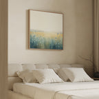A minimal, neutral-toned bedroom with a beige upholstered bed, cream bedding, and the Meadow Whispers Canvas Art - Square above the headboard, displaying blue, green, and yellow hues in an impressionistic landscape style.