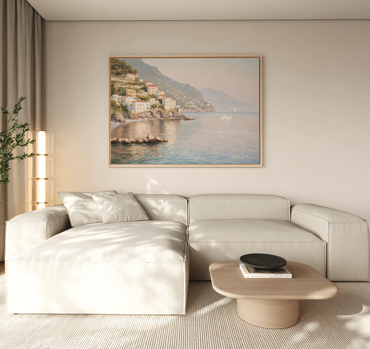 A modern living room with a light beige sectional, round wooden coffee table, and serene decor is highlighted by the Mediterranean Dreams Canvas Art - Horizontal of a coastal town above the sofa on a neutral wall.