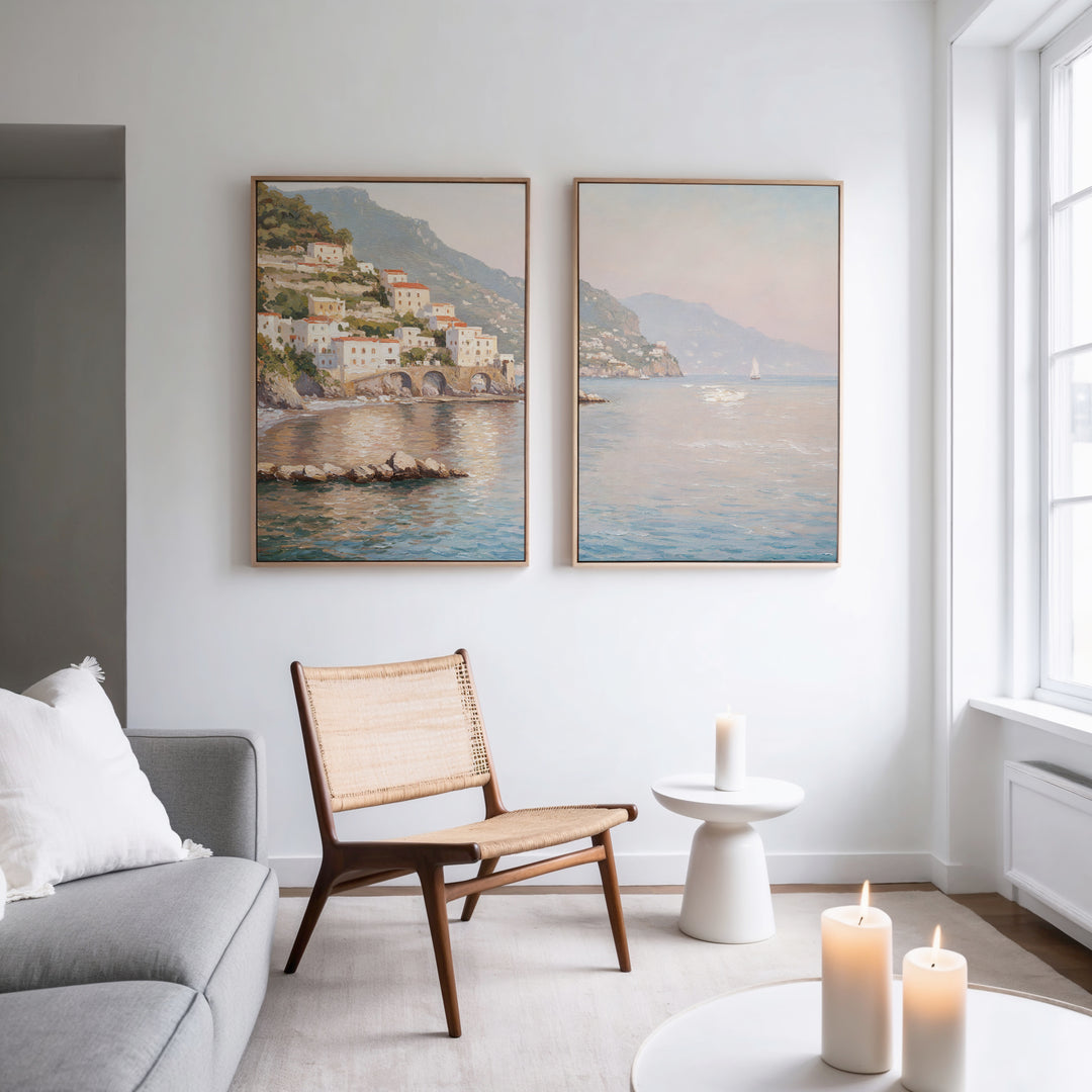 A modern, bright living room with a gray sofa, wooden chair, and white side table features lit candles and serene decor. Above, "Mediterranean Dreams - Set of 2" wall art adds coastal charm as natural light pours in through a large window.